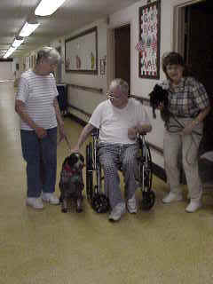 A therapy dog resting beside a person in a wheelchair while two handlers stand nearby